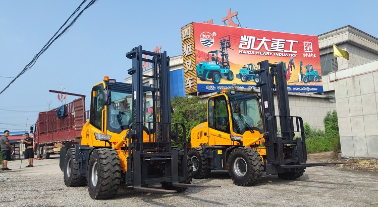 A photo showing two Kaystar all-terrain forklifts loading in a factory. The color of the forklift is yellow. The Kaystar factory is in the background. There is a Kaystar logo and text above the photo.