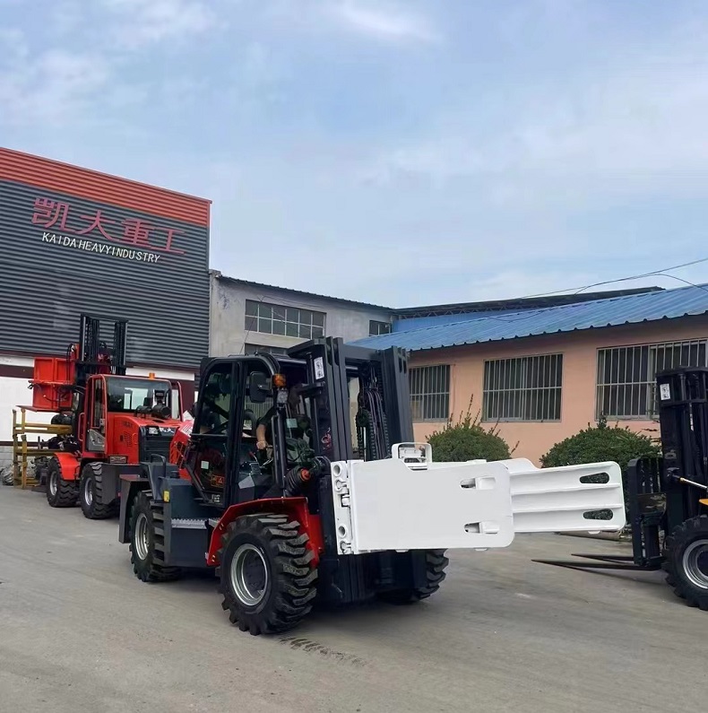 A red Kaystar articulated outdoor all-terrain forklift with a flat clamp on the front and a 3-level free-lifting mast on the back. There is the Kaystar logo on the body, and the Kaystar factory is in the background.