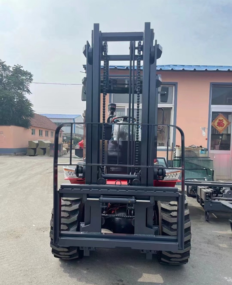 A photo of a red articulated four-wheel drive mini forklift with a rated load of 3 tons and a body width of 1.5 meters. The forklift is parked on a dirt road surrounded by trees and plants.（front view）