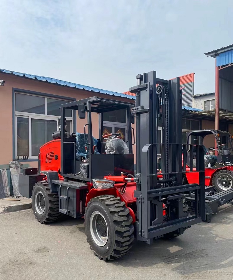 A photo of a red articulated four-wheel drive mini forklift with a rated load of 3 tons and a body width of 1.5 meters. The forklift is parked on a dirt road surrounded by trees and plants.（right side view）