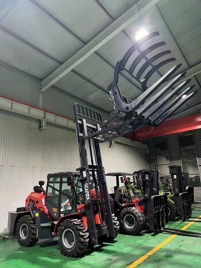 A photo of a red forklift with a black grab bucket attached to its forks, grabbing a pile of grass on a farm.