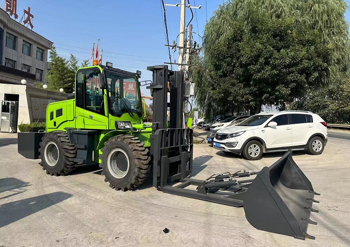 A picture of a green Landtigger50 four-wheel drive all-terrain forklift with a rated load of 5 tons, a quick-change bucket, and high-tread pneumatic tires. The forklift is waiting for transportation on a paved road with buildings in the background.